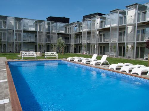 a large swimming pool with lounge chairs in front of a building at Kolgården - Visby Lägenhetshotell in Visby
