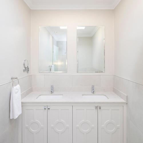 a white bathroom with two sinks and a mirror at The Plettenberg Hotel in Plettenberg Bay