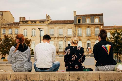 four people sitting on a wall looking at a building at FirstName Bordeaux, Part of JdV by Hyatt in Bordeaux