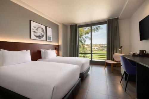 a hotel room with two beds and a desk and a window at Dolce by Wyndham Barcelona Resort in Sant Esteve Sesrovires