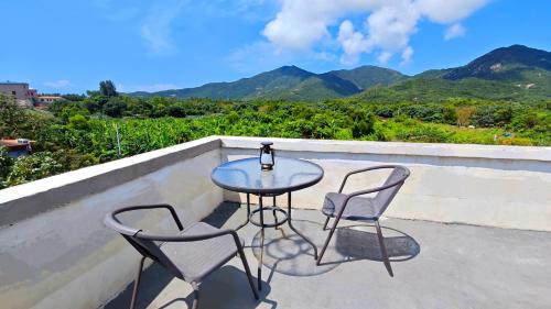 a table and two chairs on a balcony with mountains at Cloud Tree Inn Boutique Guesthouse XiChong DaPeng ShenZhen 深圳大鹏西涌云树里民宿Yun Shu Li in Shenzhen