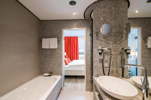 a bathroom with a tub and a sink and a bed at Steigenberger Hotel Bielefelder Hof in Bielefeld