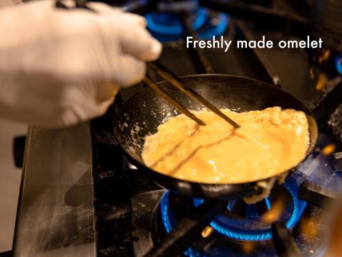 a person cooking food in a wok on a stove at Hotel Naturwald Furano in Furano