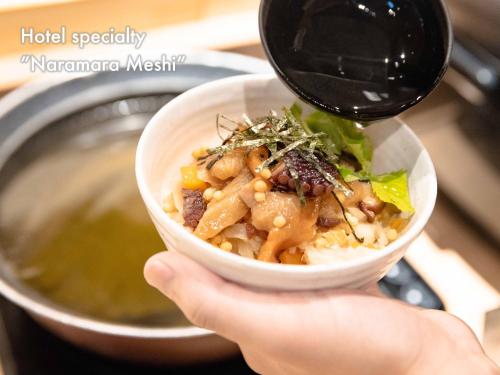 a person holding a bowl of food in front of a microwave at Hotel Naturwald Furano in Furano