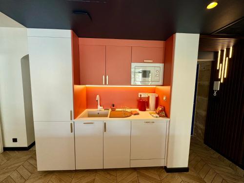a kitchen with white cabinets and an orange wall at Roma Divine home cinéma et jardin in Nîmes