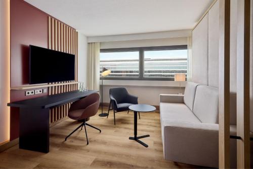 a living room with a couch and a desk with a television at Sheraton Frankfurt Airport Hotel & Conference Center in Frankfurt/Main
