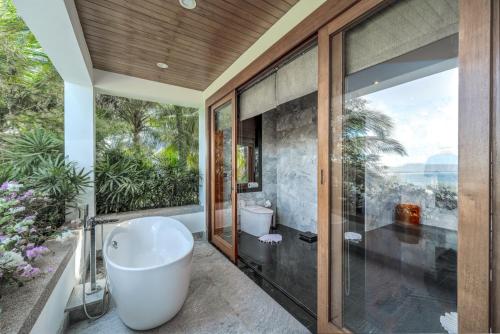 a bathroom with a bath tub and a window at Baan Phu Prana Boutique Villa in Surin Beach