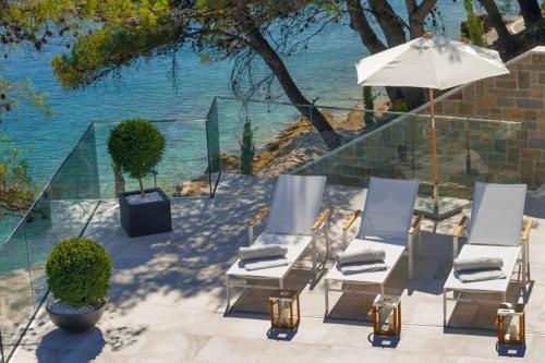 a group of chairs and an umbrella next to the water at Luxury Seafront Villa Prestige Brac with private pool, sauna and gym and private sea deck at the beach on Brac island in Selca