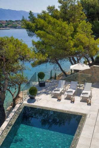 a swimming pool with chairs and an umbrella and the water at Luxury Seafront Villa Prestige Brac with private pool, sauna and gym and private sea deck at the beach on Brac island in Selca