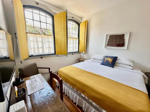 a small bedroom with a bed and two windows at Casa Simone Pousada in Paraty