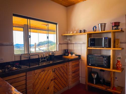 a kitchen with a sink and a microwave and a window at Chalé Vista do Paraíso in Gonçalves