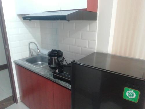 a small kitchen with a sink and a black refrigerator at Apartemen Transpark Cibubur by Royal Home in Depok