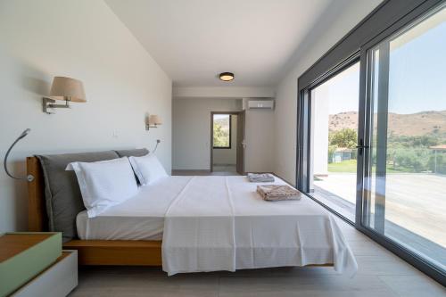 a bedroom with a large bed and a large window at Villa & Stone House with Pool, 10 Mins to Skala Eressos Beach in Eresos