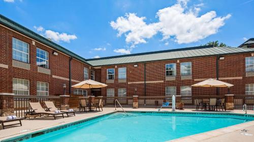 a pool with chairs and umbrellas in front of a brick building at Best Western Plus Addison/Dallas Hotel in Addison