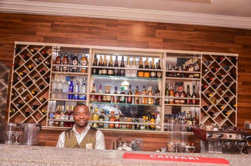 a man standing behind a bar with alcohol bottles at Danag Apartments in Port Harcourt