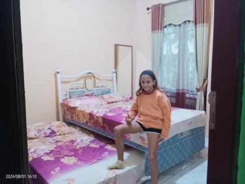 a young girl is sitting on two beds at Petra Homestay Bangka Leda in Ruteng