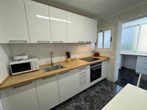 a kitchen with white cabinets and a sink and a microwave at Alojamiento Barbastro in Salou