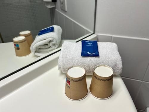 a bathroom with towels and two cups on a sink at Brit Hotel Confort Montauban in Montauban