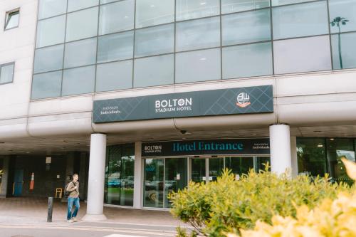 a man walking in front of a building at The Bolton Stadium Hotel, a member of Radisson Individuals in Bolton