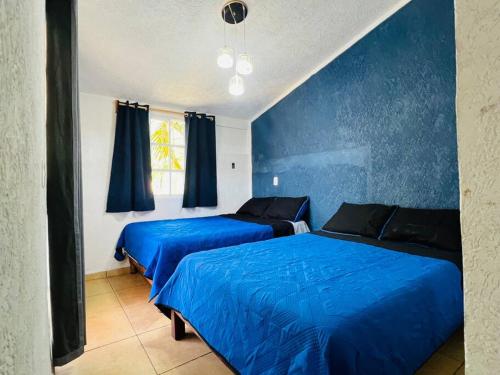 Dos camas en un dormitorio con paredes azules. en Casa a 7 min de playa, en Ixtapa