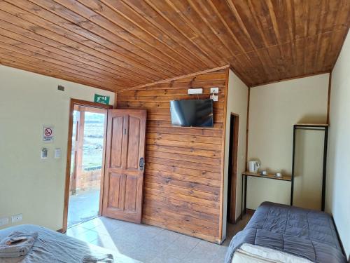 a bedroom with a wooden wall with a bed and a tv at Hosteria Lago Sur in El Calafate