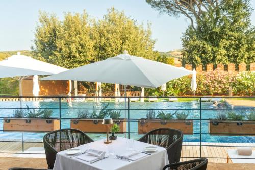 a table with chairs and an umbrella next to a pool at Borgo Dei Conti Resort Relais & Chateaux in Monte Petriolo