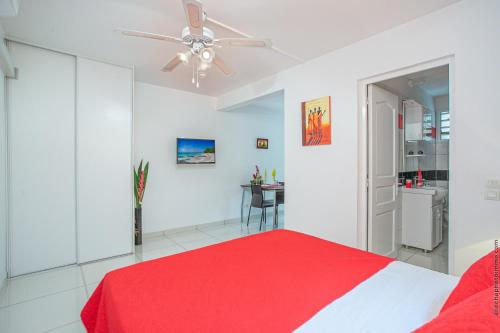 une chambre blanche avec un lit rouge et un ventilateur de plafond dans l'établissement Ixora au Refuge de Madiana à Schoelcher, à Schœlcher