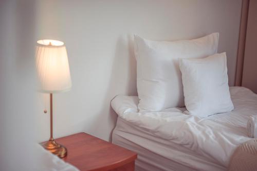 a bed with white pillows and a lamp on a table at Hotel Maxim Kwidzyn in Kwidzyn