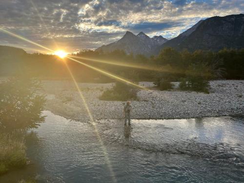 a sunset over a river with the sun setting in the mountains at OUTSCAPE l Hermosa Cabaña familiar en Cerro Castillo in Villa Cerro Castillo