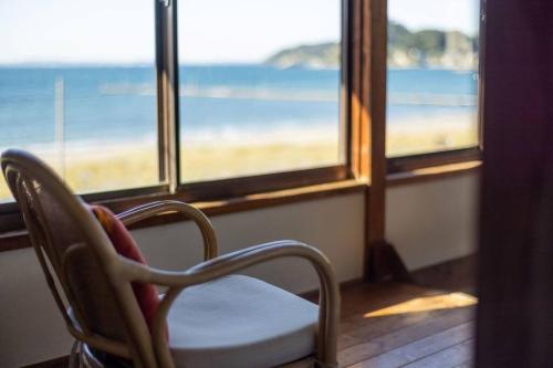 a chair in front of a window with a view of the beach at 砂浜まで10秒 海と桟橋を一望できるHaraoka House in Minamiboso