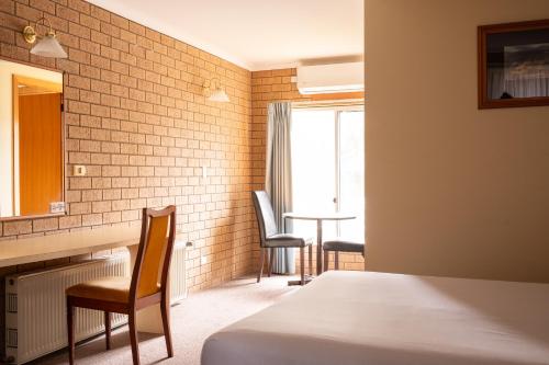 a bedroom with a bed and two chairs and a mirror at Hepburn Springs Motor Inn in Hepburn Springs