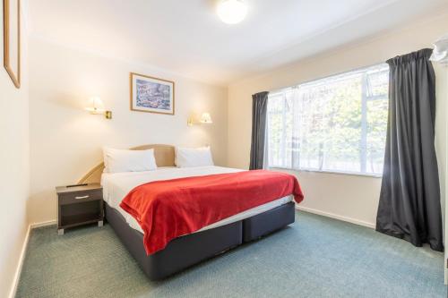 a bedroom with a bed with a red blanket and a window at ASURE PRINCE motor lodge in Taupo