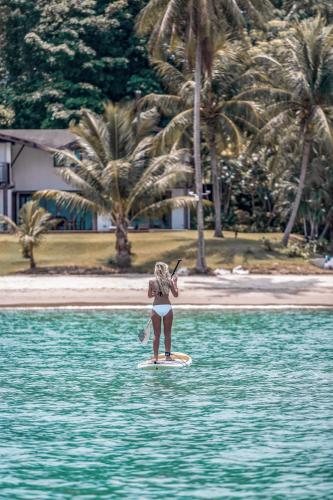 a girl is standing on a surfboard in the water at Barcelo Coconut Island, Phuket in Phuket Town