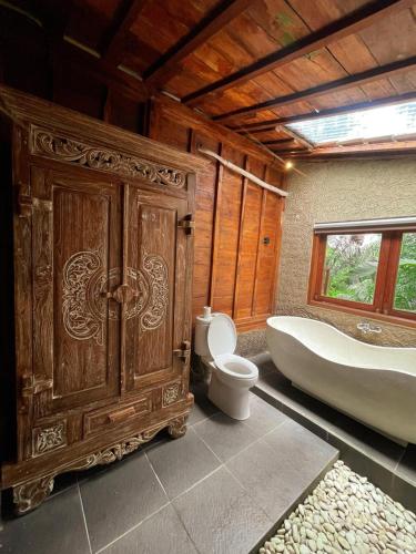 a bathroom with a large wooden cabinet and a toilet and a tub at Umah Tamu Villa in Penginyahan