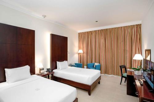 a hotel room with two beds and a desk at Metropolitan Al Mafraq Hotel in Abu Dhabi