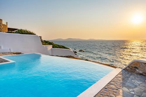 a swimming pool next to the ocean at sunset at Villa Coventina in Agios Ioannis Mykonos