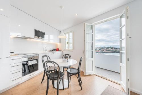 a kitchen with white cabinets and a table with chairs at GuestReady - Riverview Douro Balcony in Vila Nova de Gaia