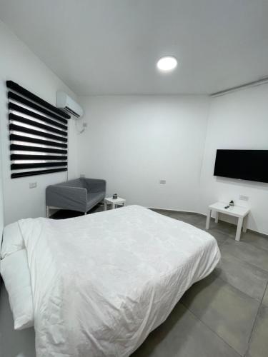 a white bedroom with a bed and a flat screen tv at Zan in Netanya