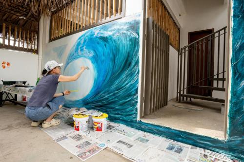 a woman painting a painting of a wave on a wall at The Circle Hostel, La Union in San Fernando