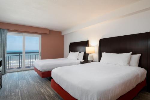 two beds in a hotel room with a balcony at Hilton Garden Inn Daytona Beach Oceanfront in Daytona Beach