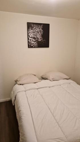 - un lit avec des draps blancs et une photo sur le mur dans l'établissement Appartement meublé, à Roubaix