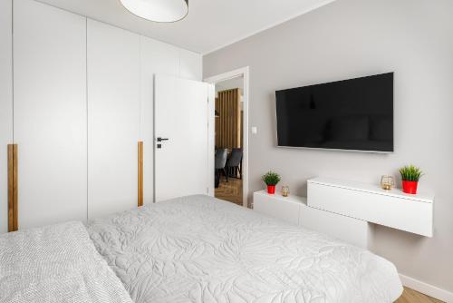 a white bedroom with a bed and a flat screen tv at Apartament Stacja Wisła in Wisła
