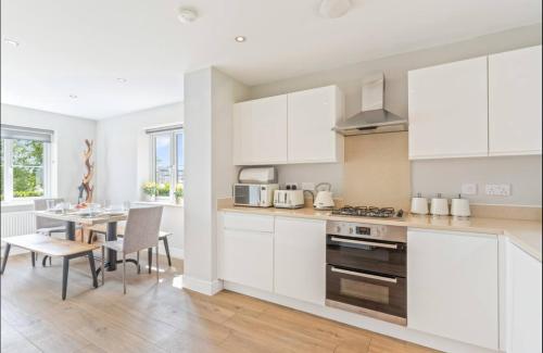 a kitchen with white cabinets and a table with chairs at Luxury 5 bed house with Hot Tub nr Bicester Village in Bicester