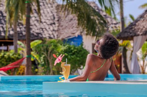 une femme assise dans une piscine avec un verre dans l'établissement TIANDE Boutique Hotel, à Pwani Mchangani