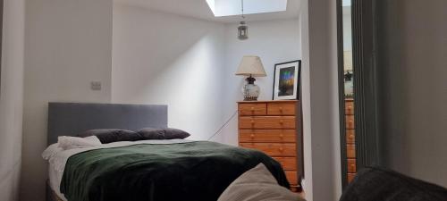 a bedroom with a bed with a green blanket and a dresser at King's Cross Road Private Rooms in London
