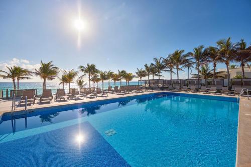 a swimming pool with chairs and palm trees at Riu Palace Kukulkan - Adults Only - All Inclusive in Cancún