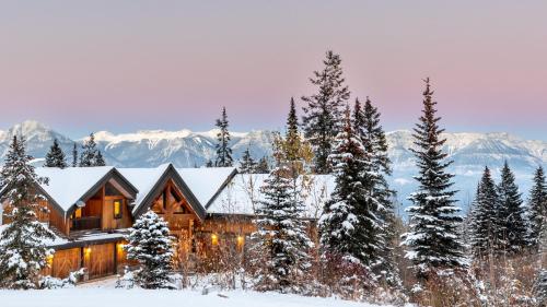 a log cabin in the snow with mountains in the background at Lush Mountain Accommodations in Golden