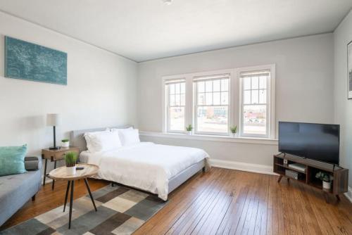 a white bedroom with a bed and a flat screen tv at CITY VIBES - Modern Suite in the heart of Downtown in Peoria