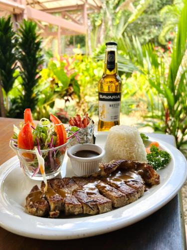 a plate of food with meat and a bottle of beer at Ávita Lodge in Quesada