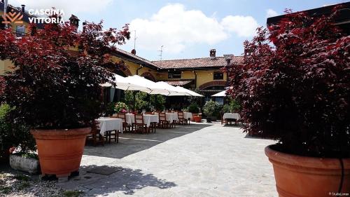 a patio with tables and chairs and white umbrellas at Cascina Vittoria Restaurant Lab & Rooms in Rognano